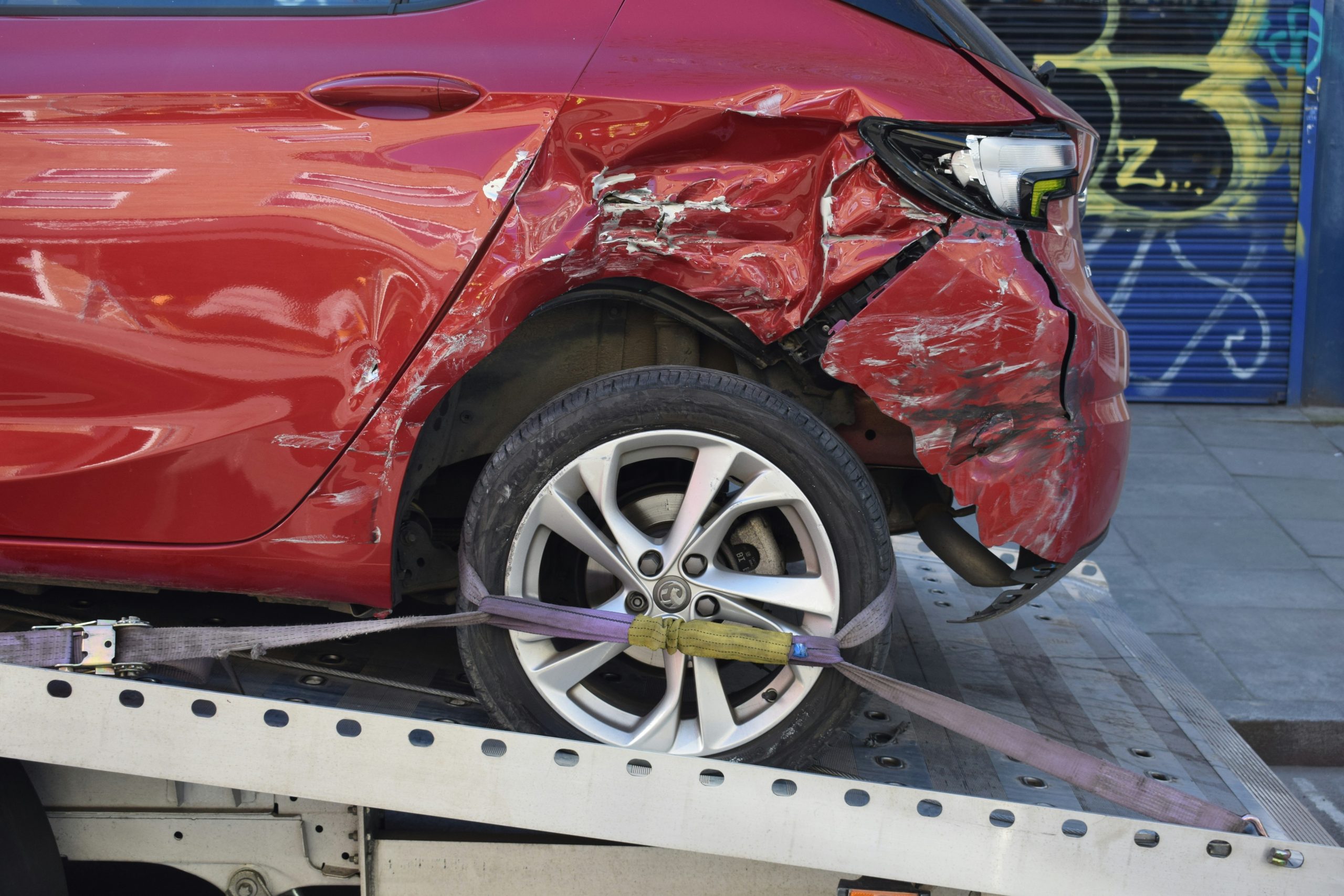 Towing company near me, Experienced tow operator securing damaged sedan with proper recovery equipment and straps, Tow truck loading disabled sedan outside shopping center after sudden daytime breakdown